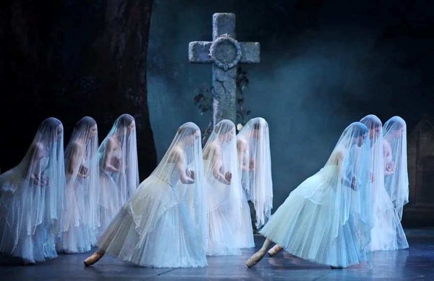 Un groupe de danseuses voilées de tulle rassemblées devant une croix de pierre