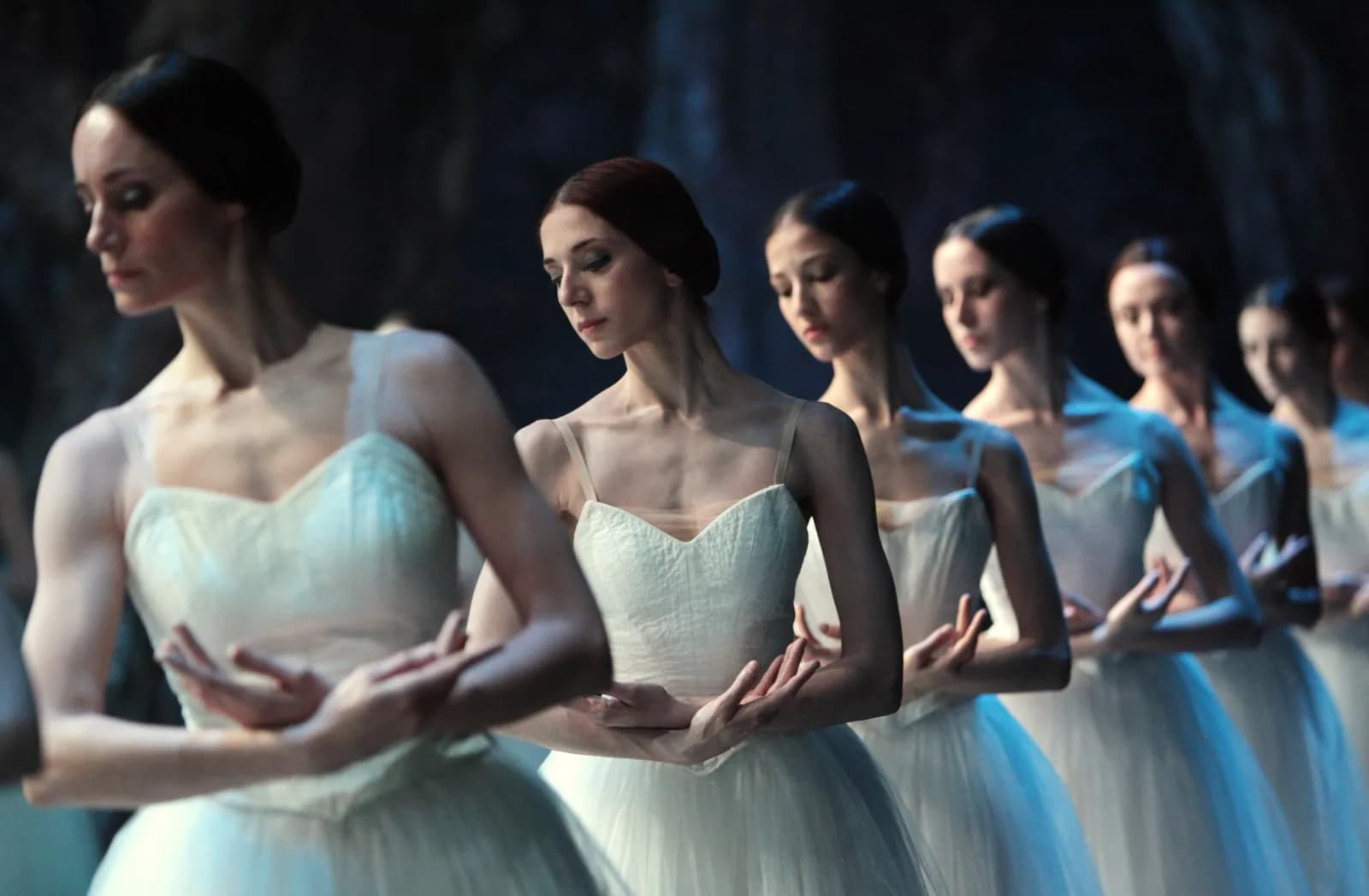 Gros plan d'une file de danseuses au regard baissé, bras croisés