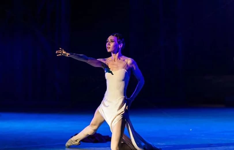 Danseuse à genoux en robe crème, bras tendu, dans un halo bleu