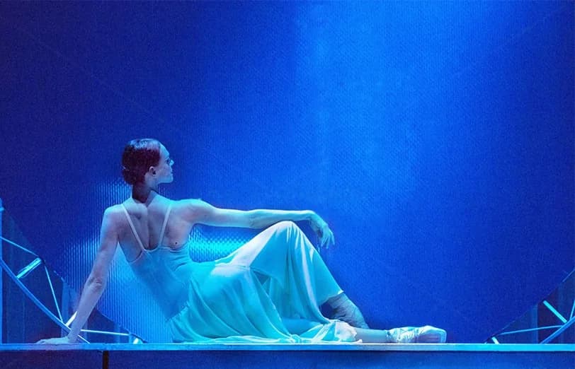 Danseuse allongée en robe fluide sur une structure basse, fond bleu