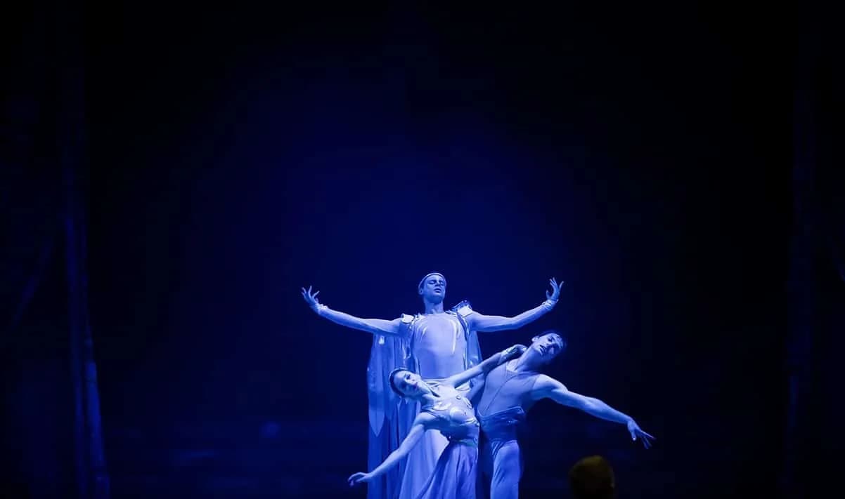 Trio de danseurs en costumes clairs émergeant de l'obscurité