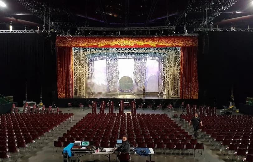 Salle vide aux fauteuils bordeaux face à un manteau de scène doré