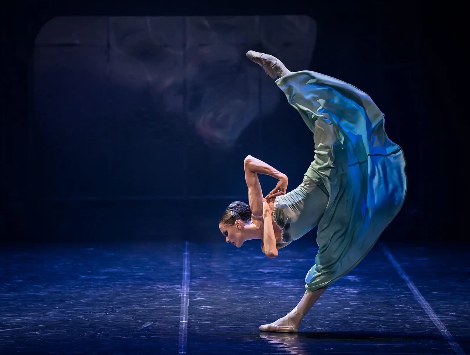 Danseuse en tunique bleu-vert pliée en avant, jambe tendue vers le ciel