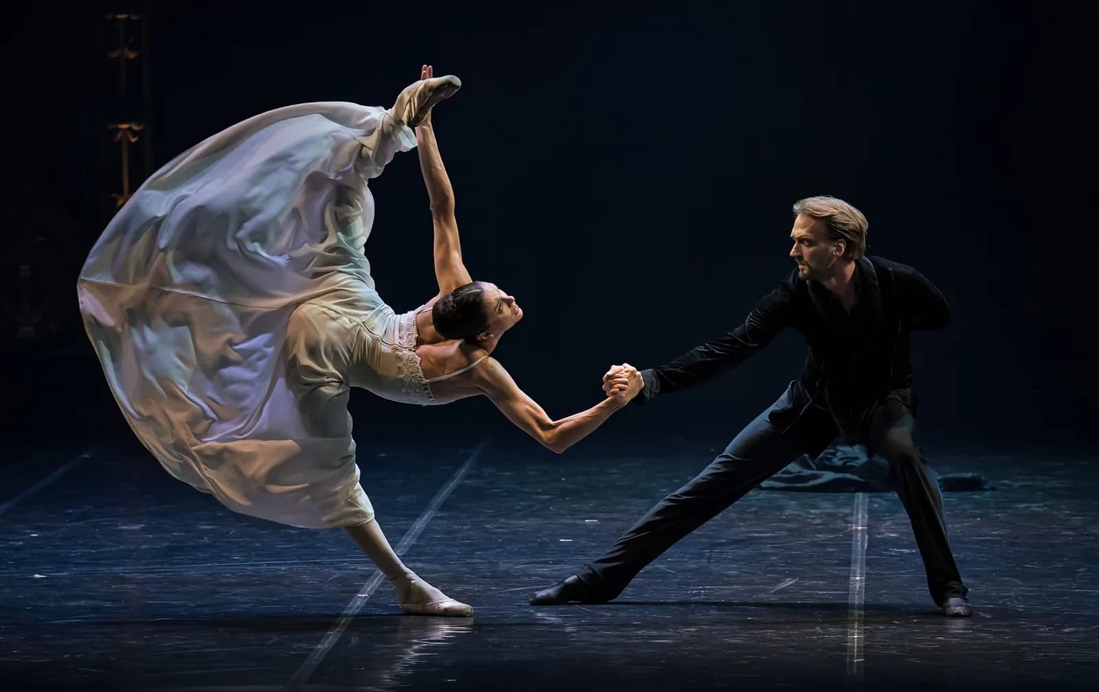 Danseuse en robe claire cambrée, voile envolé, tendant la main à un partenaire