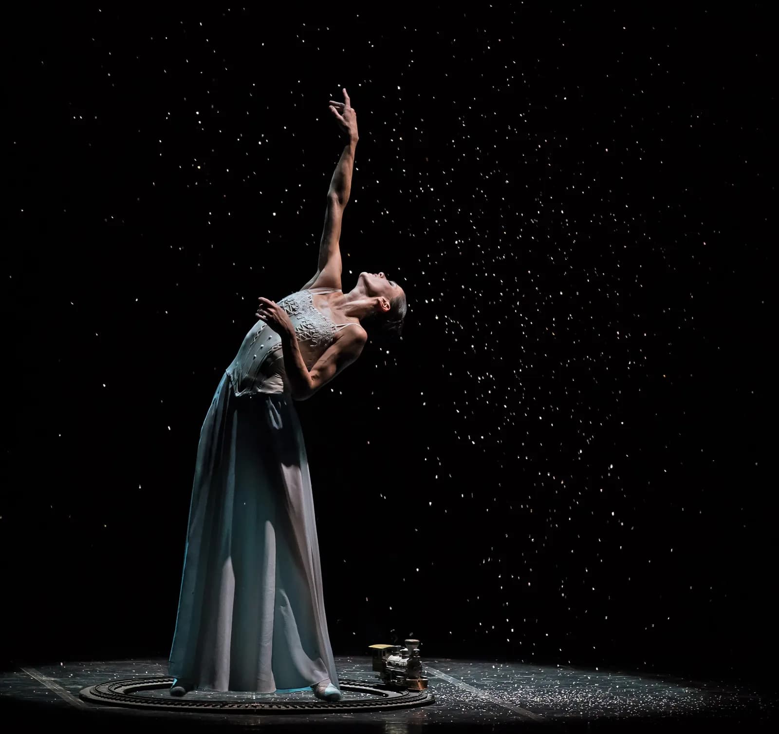 Danseuse en longue robe grise debout sur un socle rond, bras levé