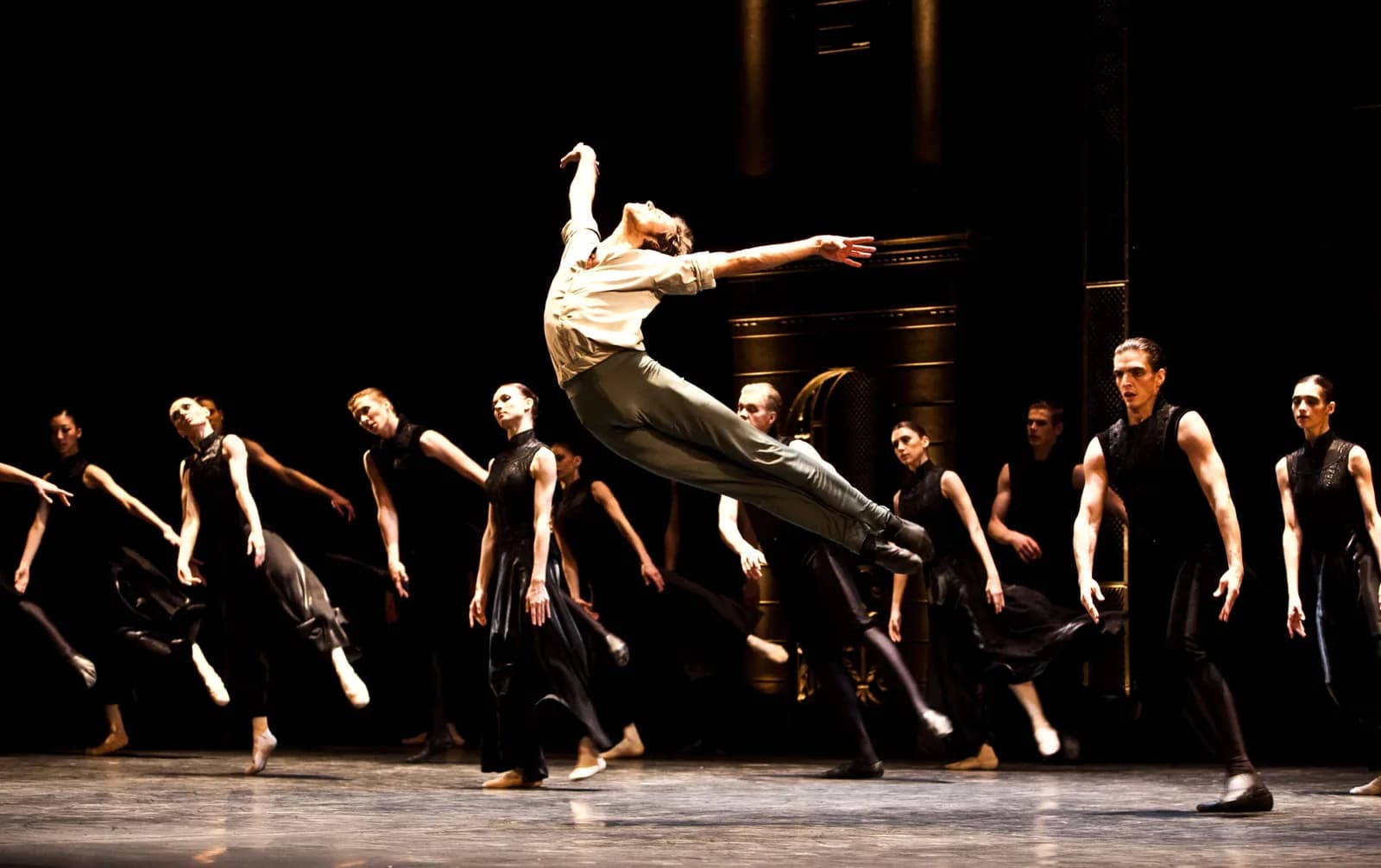 Danseur en chemise claire suspendu en plein saut devant le corps de ballet