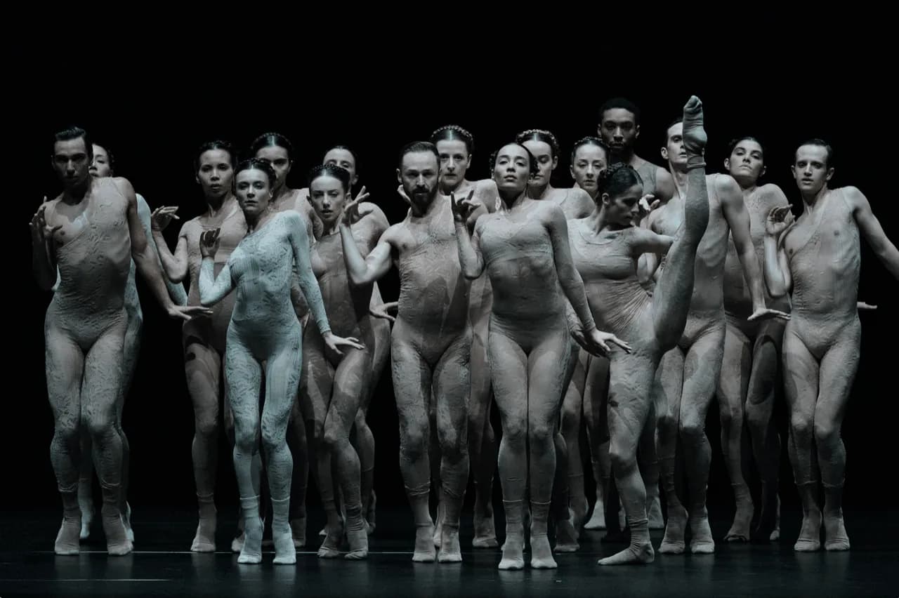 Groupe serré de danseurs au corps couvert d'argile grise sur fond noir