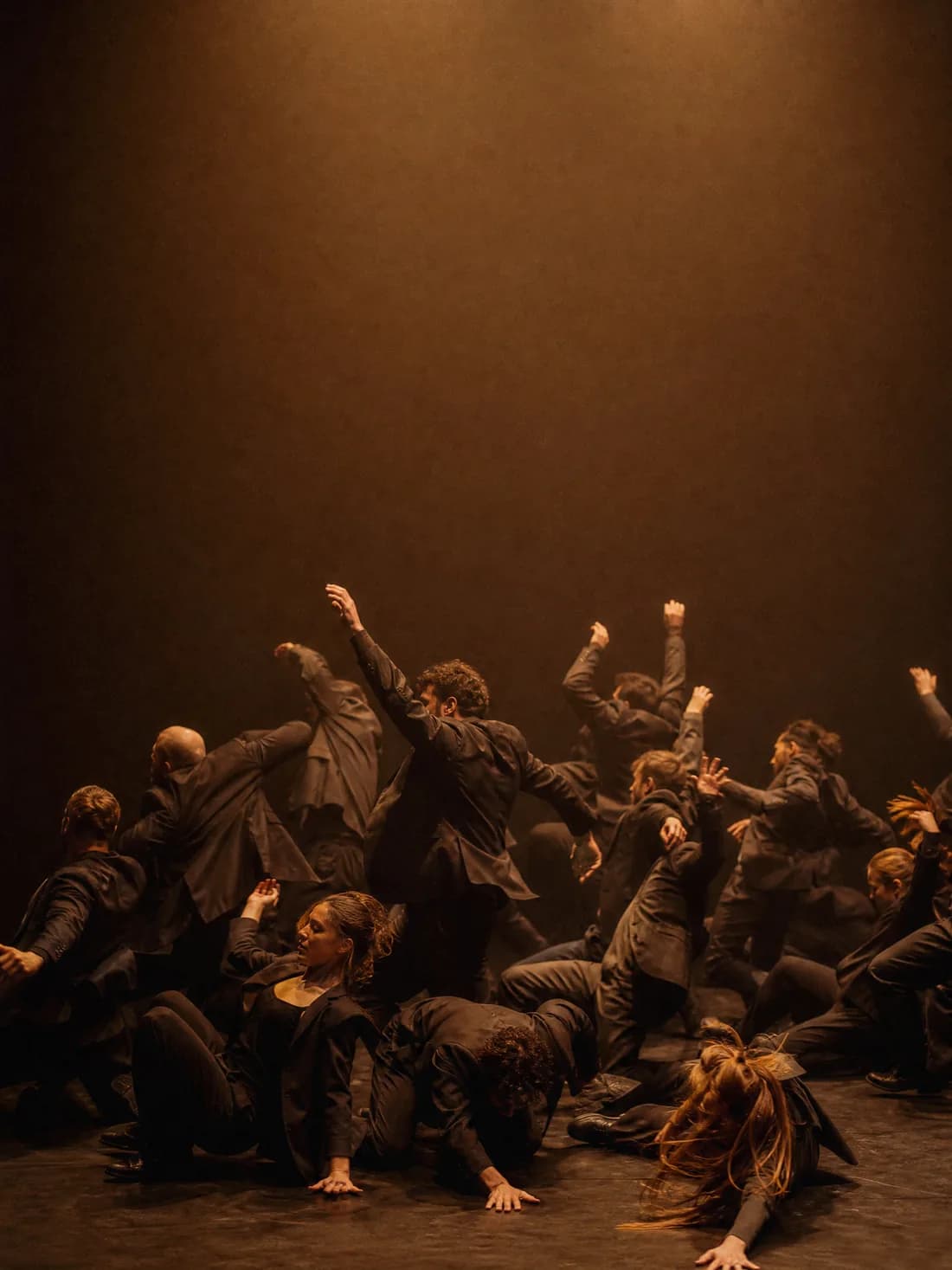 Un grand ensemble contemporain en costumes sombres saisi en pleine chute, lumière ambrée d'en haut