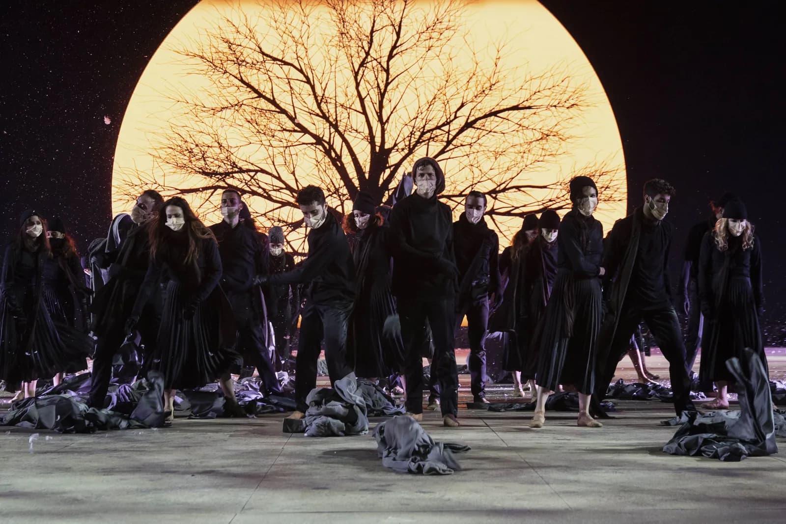 Une lune géante derrière un arbre nu, la foule en manteaux noirs