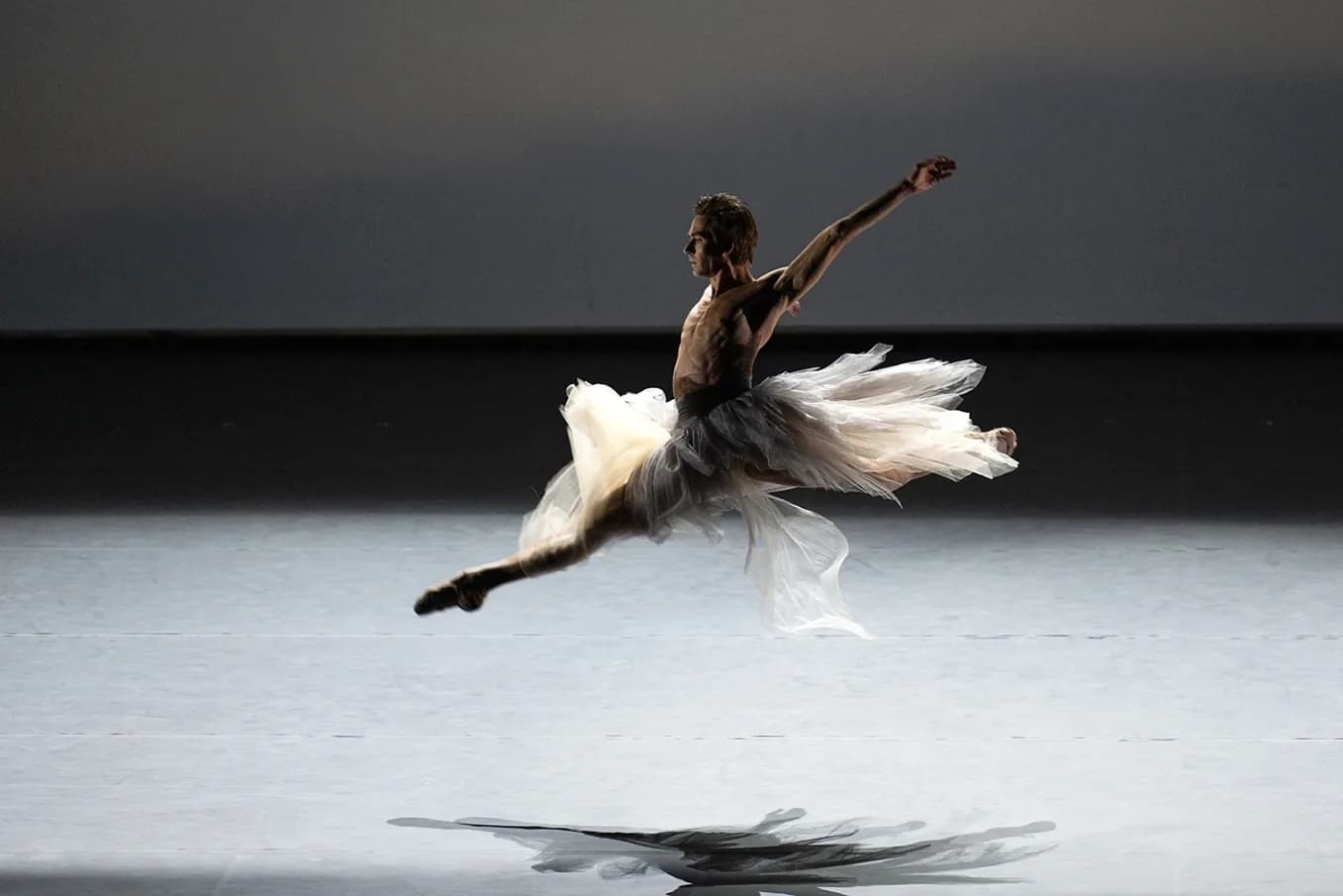 Danseuse en tutu vaporeux en plein saut devant un mur gris