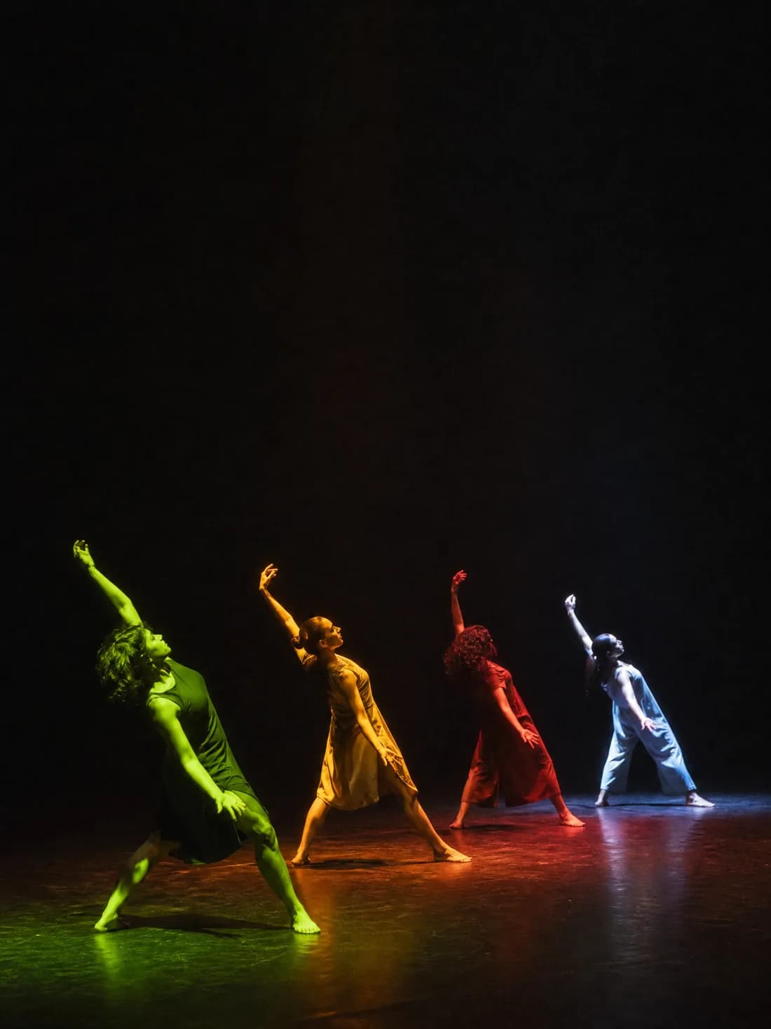 Quatre danseurs en diagonale, chacun dans une lumière de couleur différente, plateau nu