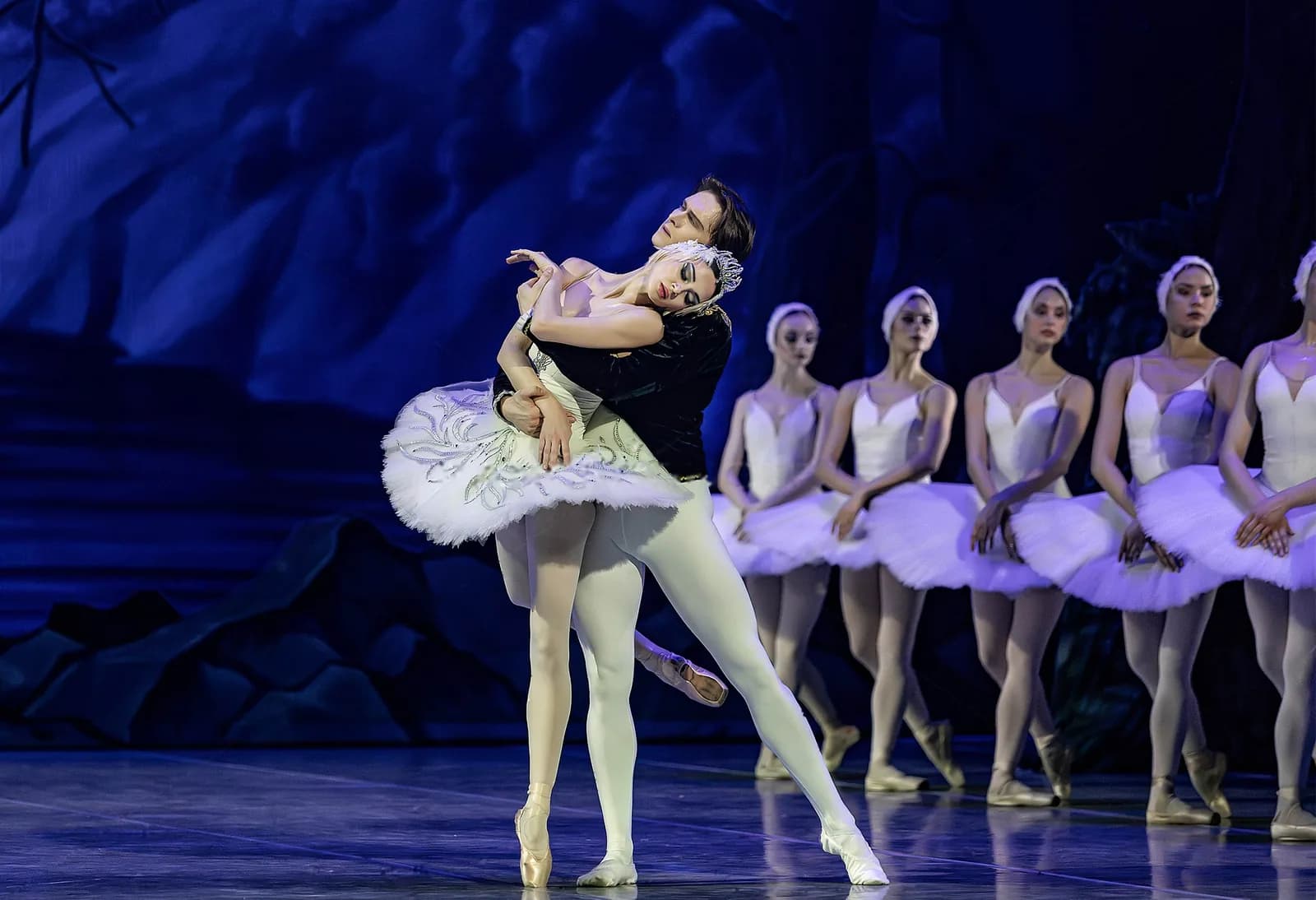 Un danseur soutient une ballerine en tutu blanc, la ligne des cygnes derrière