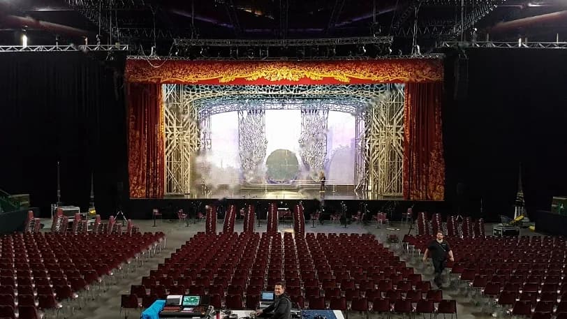 Salle vide aux fauteuils bordeaux face à un manteau de scène doré