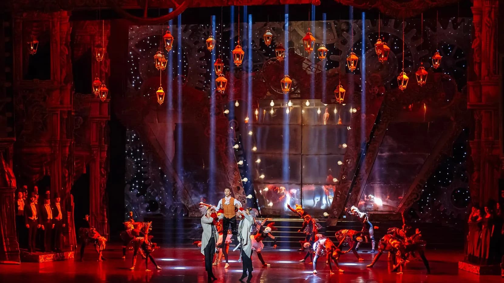 Plan large du plateau baigné de rouge, lanternes suspendues au-dessus des danseurs