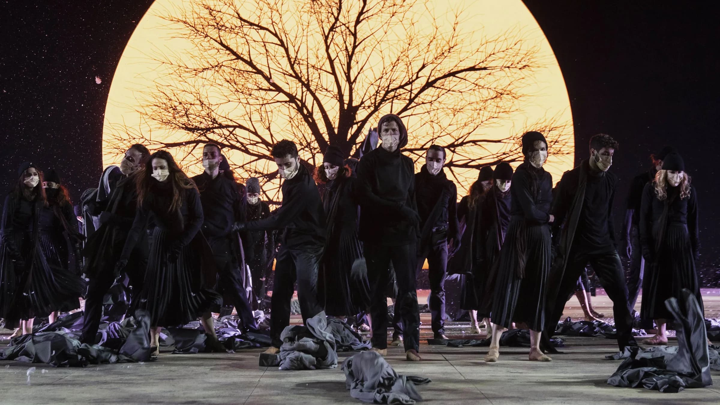 Une lune géante derrière un arbre nu, la foule en manteaux noirs