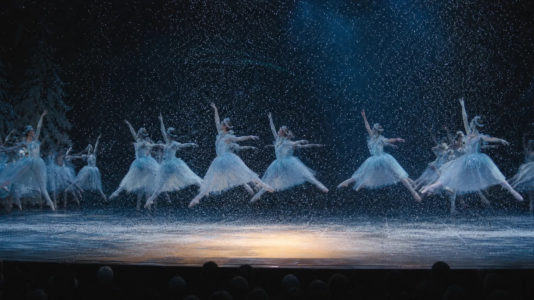 Le corps de ballet en tutus bleu pâle en plein saut sous une neige dense, lumière bleue latérale et une flaque d'or au sol