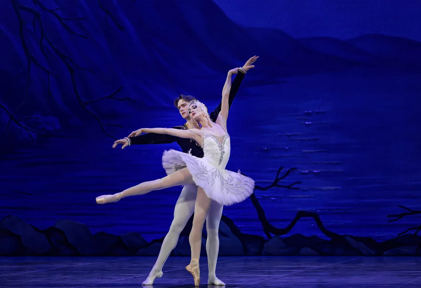 Pas de deux au bord du lac : un danseur soutient une ballerine en tutu blanc